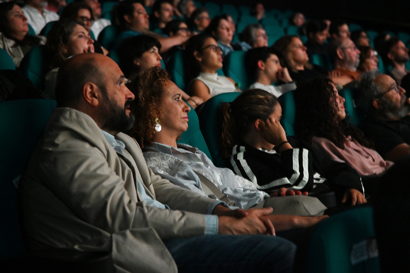 Decenas de personas sentadas en la sala de un cine ven hacia la pantalla