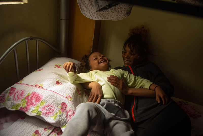 Una mujer joven y una niña pequeña, sonríen mientras están recostadas en una cama