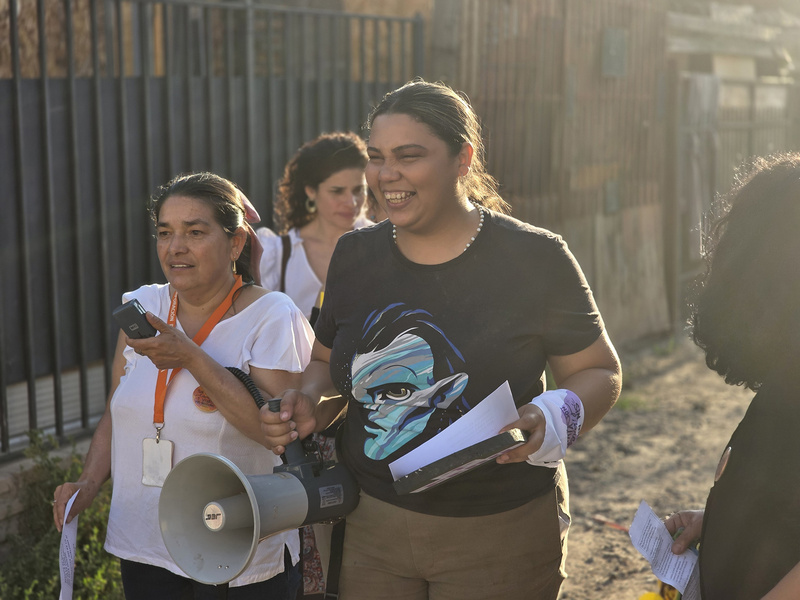 Dos mujeres distribuyen volantes en la calle ayudándose con un megáfono.