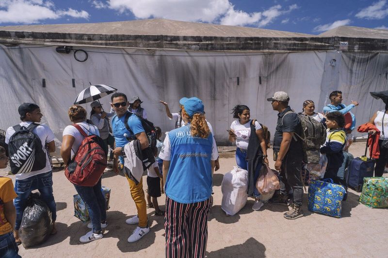 Una trabajadora de ACNUR con su chaleco y gorra de visibilidad habla con un grupo de personas en una fila.