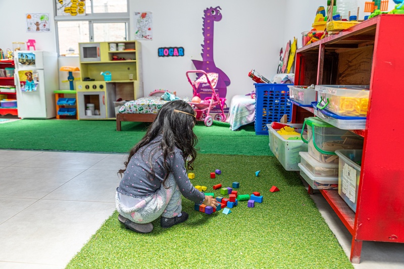 En una habitación infantil, una niña de espaldas, juega con bloques de colores
