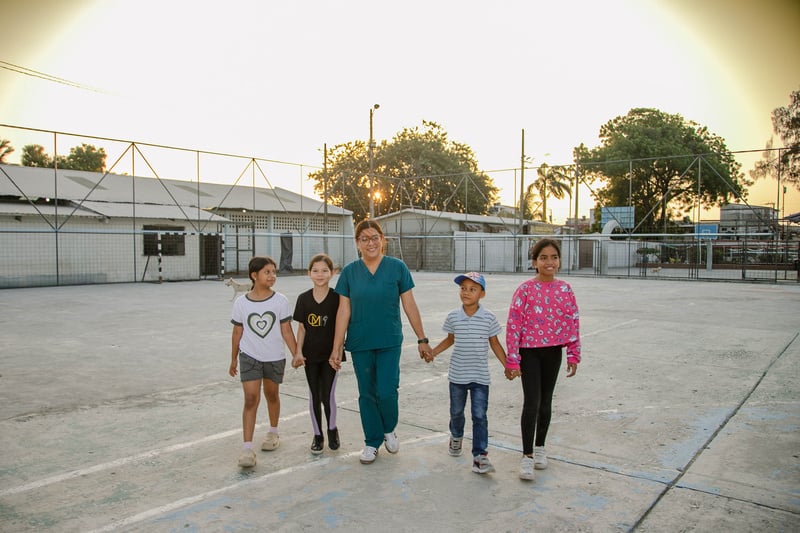 Una mujer y cuatro niños posan para una foto en una cancha deportiva.