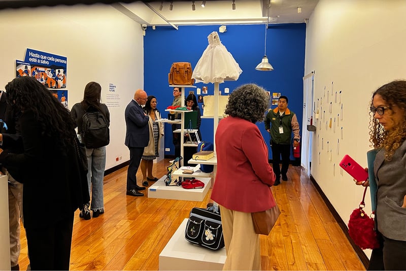 Varias personas miran una exposición de objetos personales como bolsos, cuadernos y ropa en una sala de museo.