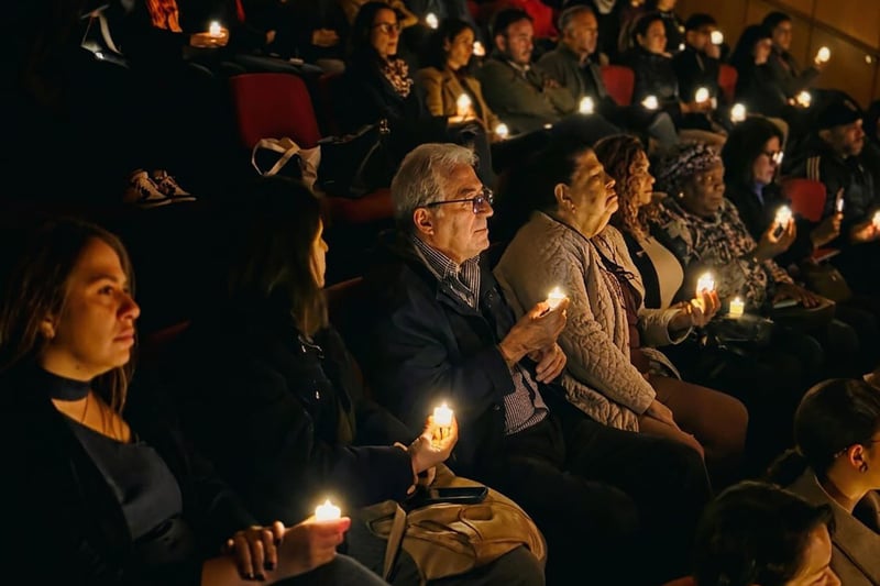 Espectadores en un auditorio con luces bajas escuchan con atención sujetando una velas led.