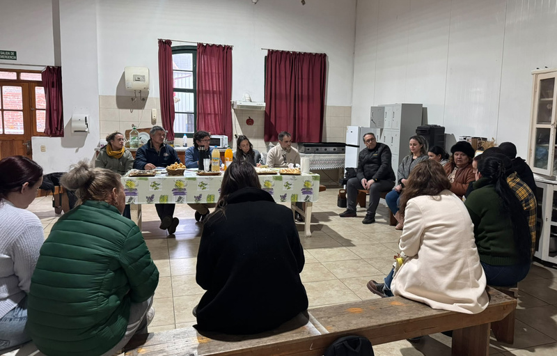 Un grupo de 17 personas sentadas en bancas al rededor de una mesa en una cocina amplia