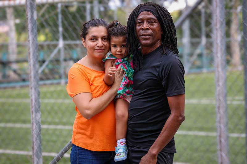 Una mujer vestida de color naranja y un hombre vestido de negro, posan junto a una niña pequeña de vestimenta colorida