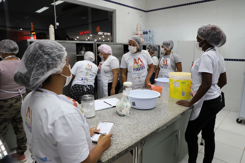 Un grupo de mujeres que llevan puestos delantales, mascarillas y gorros durante una clase de cocina.