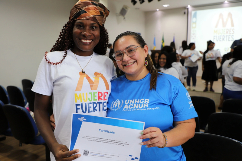 Dos mujeres sonríen para la cámara mostrando un título de formación.