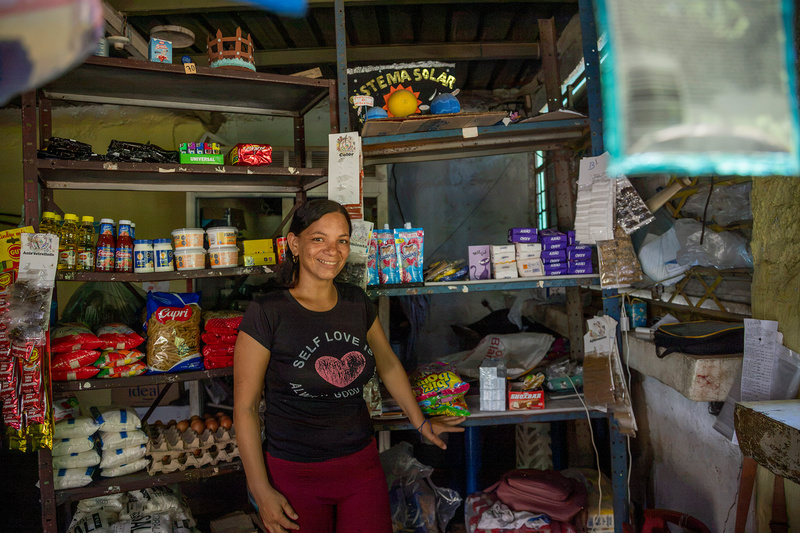 Una mujer vestida con camiseta negra y pantalón rojo, de pie dentro de una tienda de abarrotes
