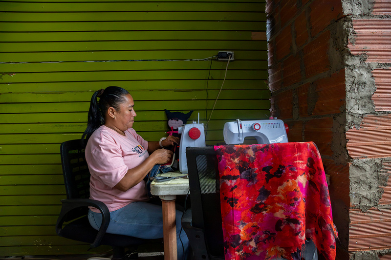Una mujer con camiseta rosa y jeans, sentada en una silla frente a una máquina de coser