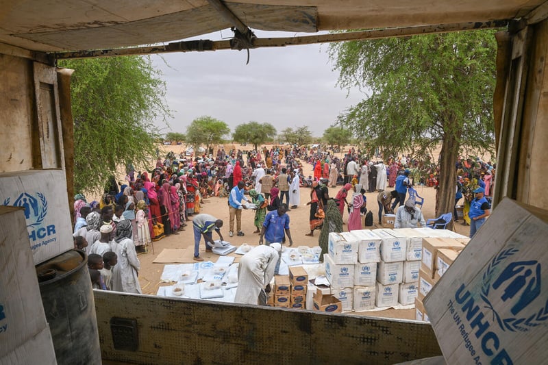 Vista desde la parte trasera de un camión que muestra a personas descargando suministros de ayuda para los refugiados que esperan cerca