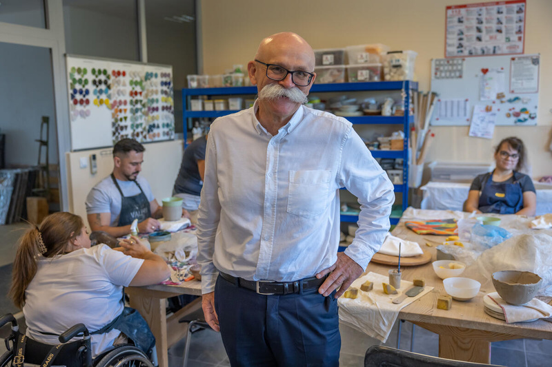 Un hombre que usa un gran bigote blanco posa en un taller de cerámica.