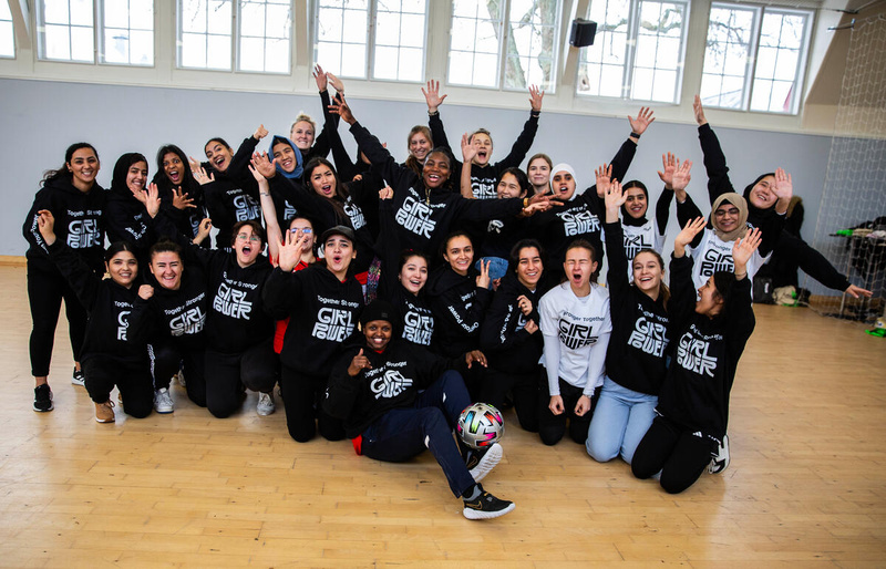 Un grupo de 30 mujeres con sudaderas negras posan para la foto en un salón de entrenamiento
