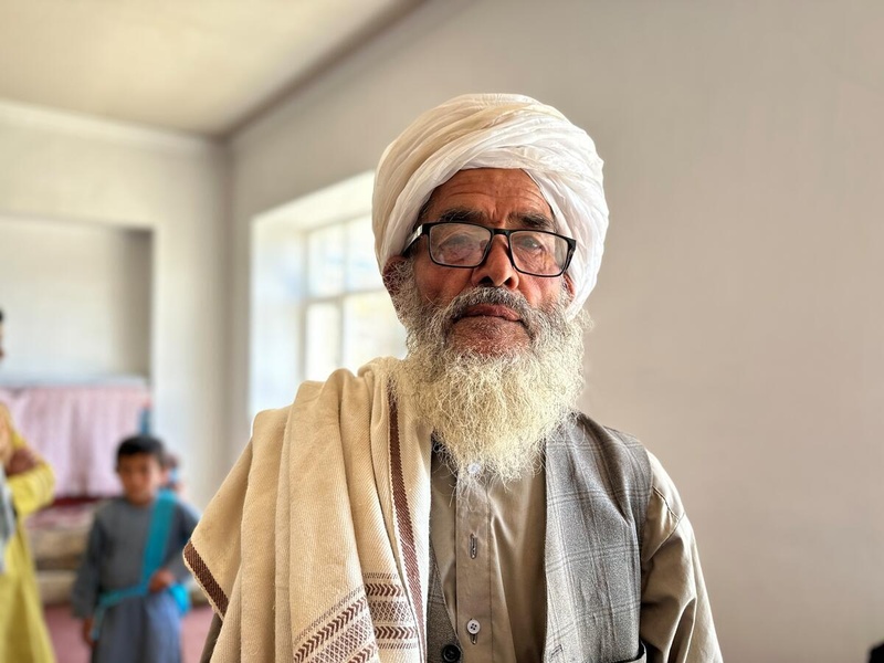 Un hombre afgano de 80 años, que lleva anteojos, tiene barba y lleva puesto un turbante color blanco, mira a la cámara con una expresión de tristeza