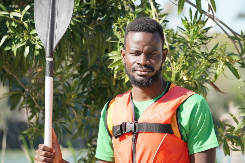 Aliou posa para una foto con su chaleco salvavidas y un remo de kayak.