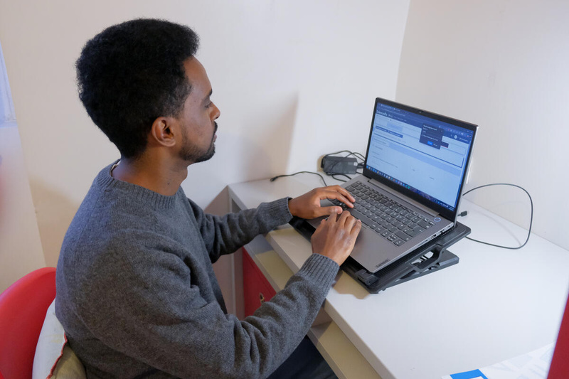 Un hombre sentado en un pequeño escritorio trabajando con una computadora portátil