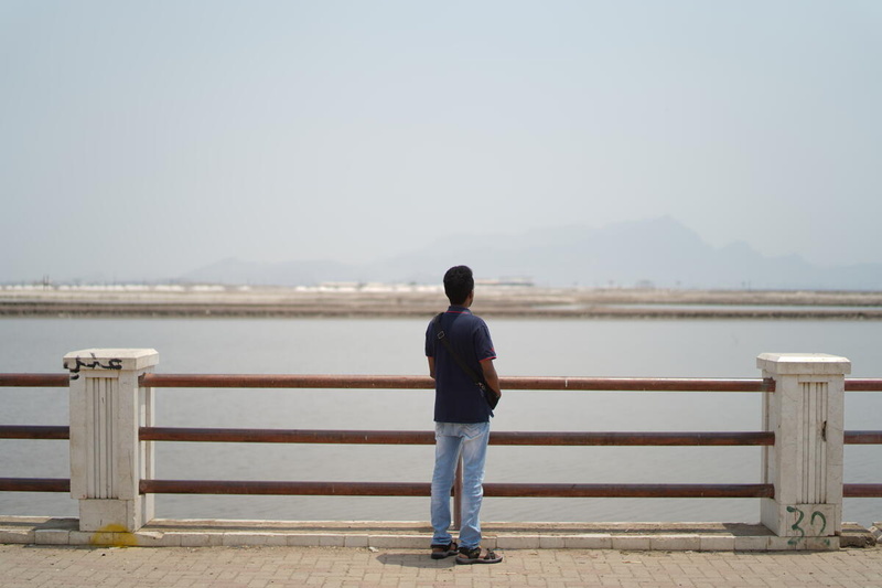 Un hombre contempla una extensa superficie de agua con una vista difusa de las montañas en la distancia