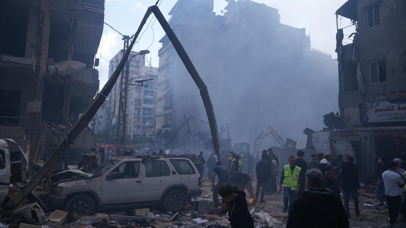 Multitudes de personas se concentran en una calle de la ciudad entre edificios y vehículos dañados, a través de una cortina de humo