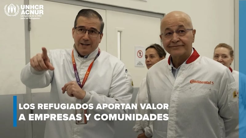 El Alto Comisionado visita la planta de Aumovio en Aguascalientes junto con el gerente de planta. Ambos llevan puesta una bata blanca y estpan conversando en un pasillo mientras caminan.
