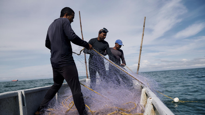 Tres hombres afro recogen una red de pesca sobre una embarcación