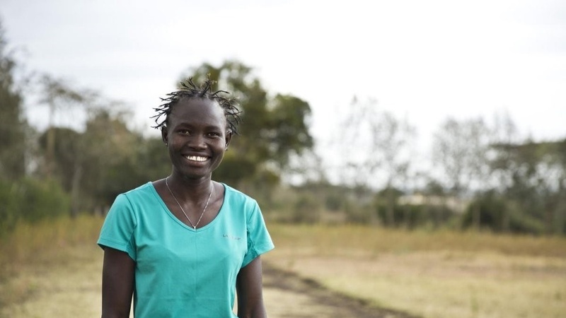 Una mujer sudsudanesa en un terreno con vegetación sonríe a la cámara