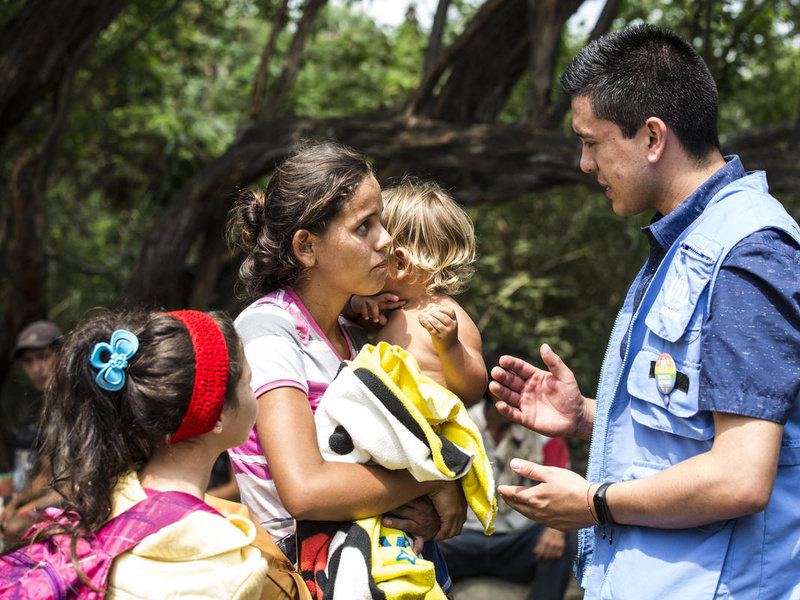 Una mujer con dos niños pequeños charla con un trabajador de ACNUR en Colombia.