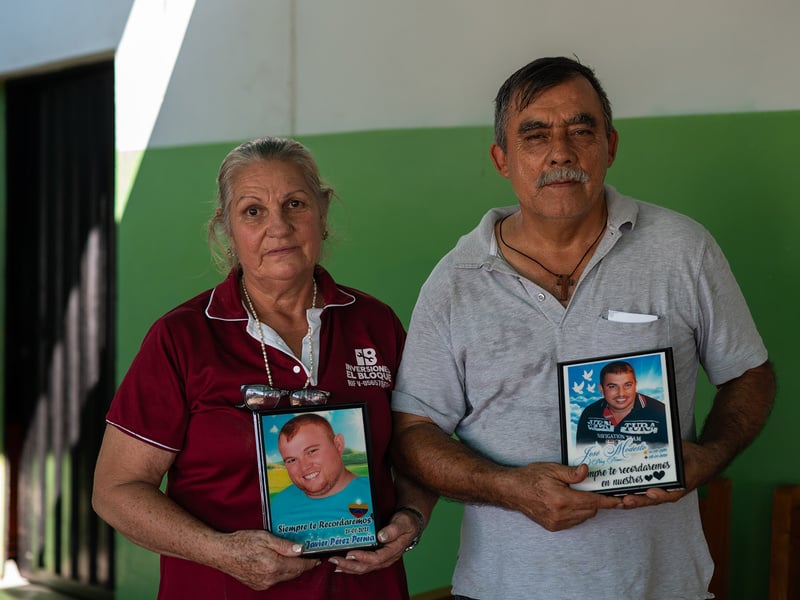 una mujer y un hombre mayores posan sujetando las fotos de dos hombres jóvenes.