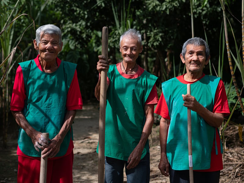 Tres hombres mayores posan sonriendo con sus herramientas de trabajo.