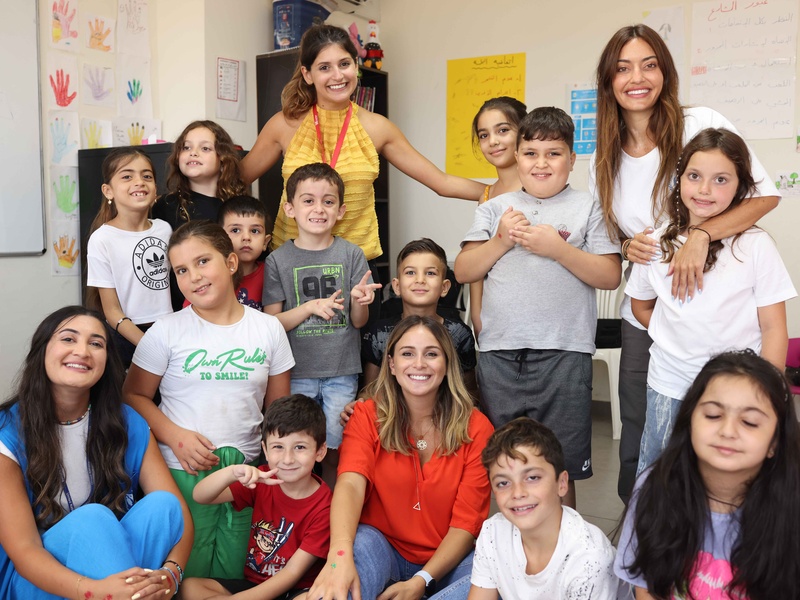 Una grupo de niñas y niños sonríen a la cámara; entre ellos, cuatro mujeres adultas.