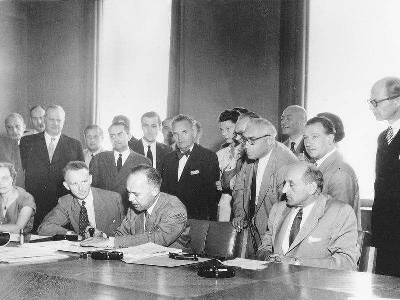 Forto en blanco negro de 20 hombres y dos mujeres firmando un documento