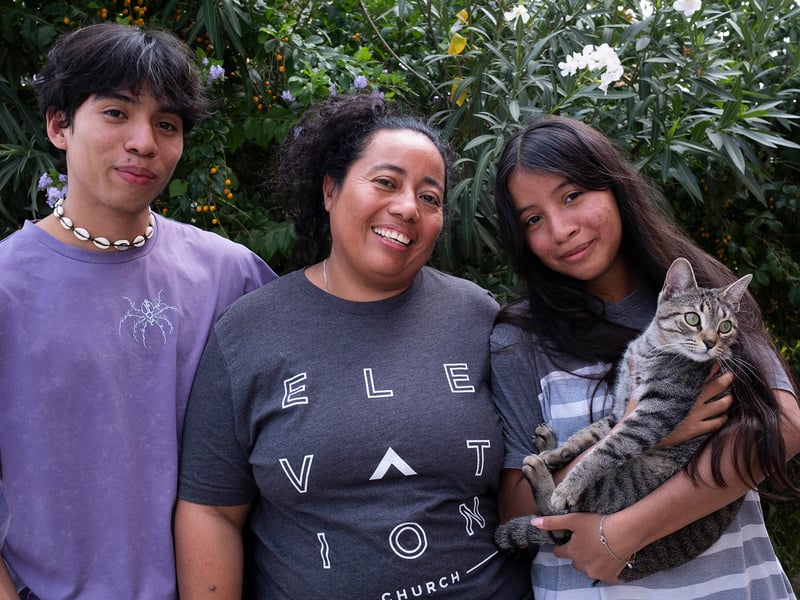 Al centro, una mujer con su hija y su hijo adolescentes. Su hija, quienestá a su lado izquierdo, sostiene entre sus brazos a un gato