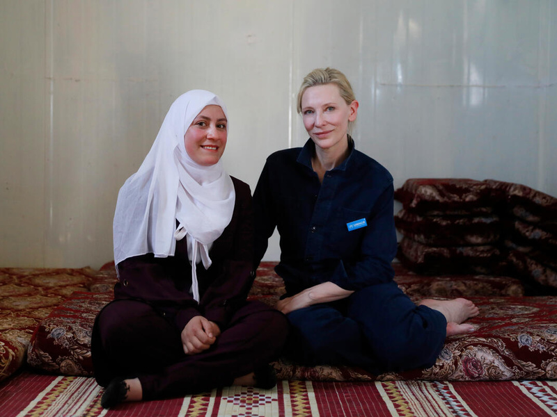 Dos mujeres sentadas en el suelo sonríen a la cámara; la que está a la izquierda, lleva puesto un hiyab color blanco.