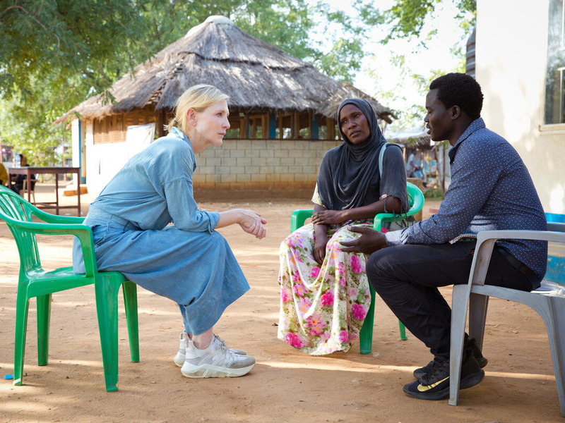 Dos personas africanas, una mujer y un hombre, charlan con una mujer rubia que está sentada frente a ellos.