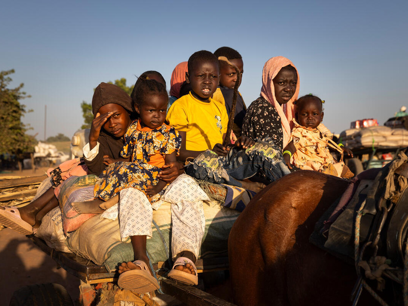 Un grupo de niños sudaneses sentados encima de un auto detrás de un caballo