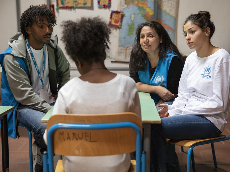 Tres mujeres y un hombre conversan; están sentados en un pequeño círculo en lo que parece un aula.