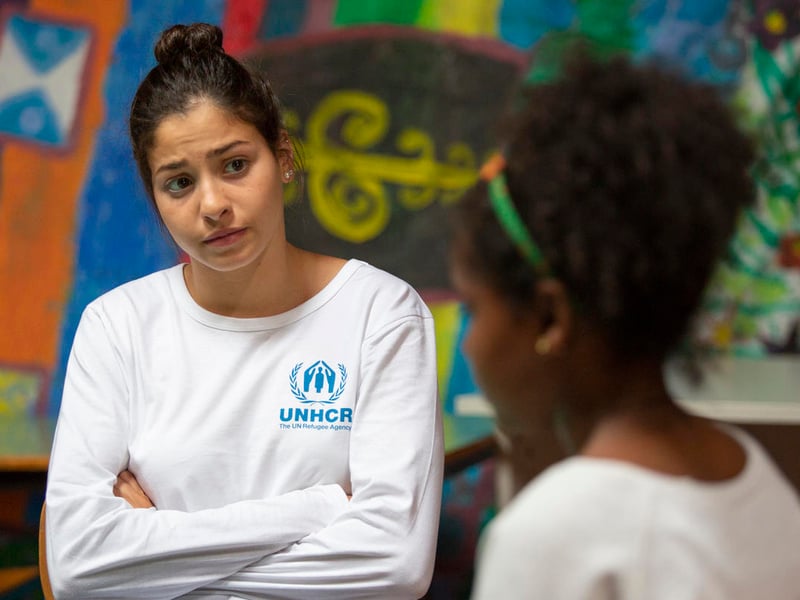 Una joven siria, que lleva puesta una camiseta blanca con el logotipo de ACNUR, escucha con atención a una joven de Eritrea.