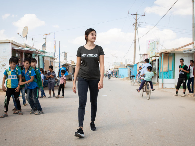 Una mujer joven camina sonriente por la calle principal de un camapmento de refugiados en Jordania