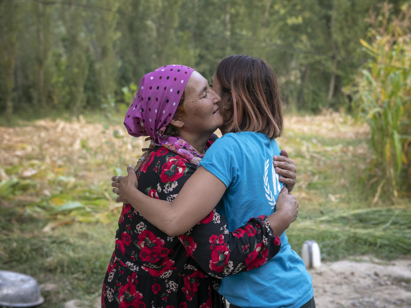 Dos mujeres, una de ellas lleva un pañuelo rojo en la cabeza, se abrazan emotivamente en medio de un área verde