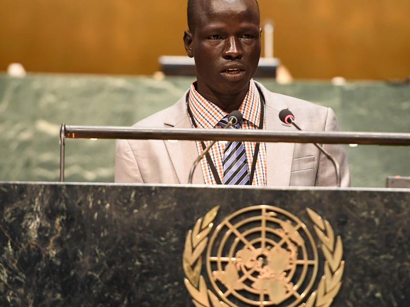 Un hombre sursudanés, que lleva puesto un traje sastre con corbata, se pronuncia desde un podio con el logotipo de la ONU.