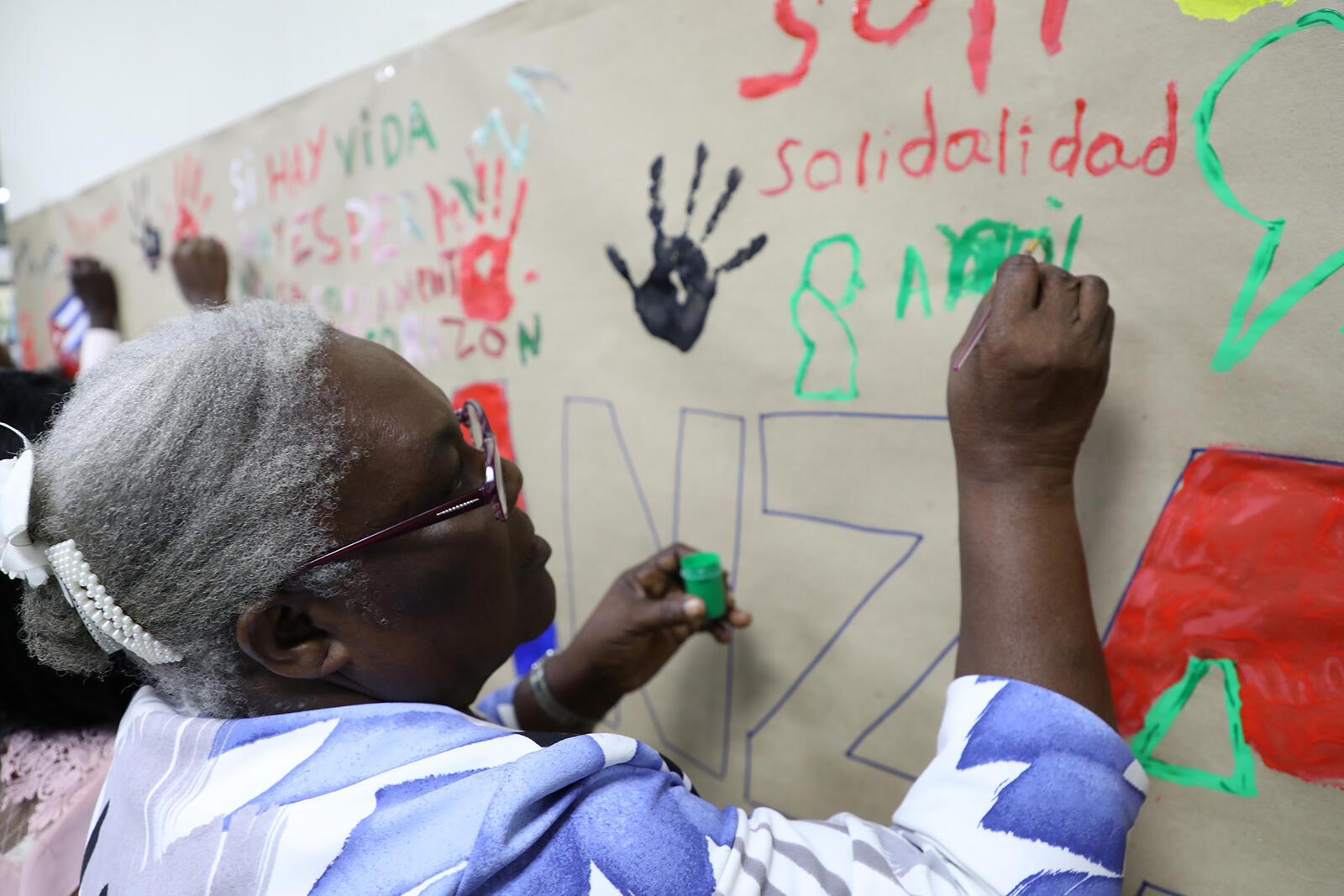 Persona refugiada de Haití pinta mural durante encuentro comunitario por el Día Mundial del Refugiado 2023.