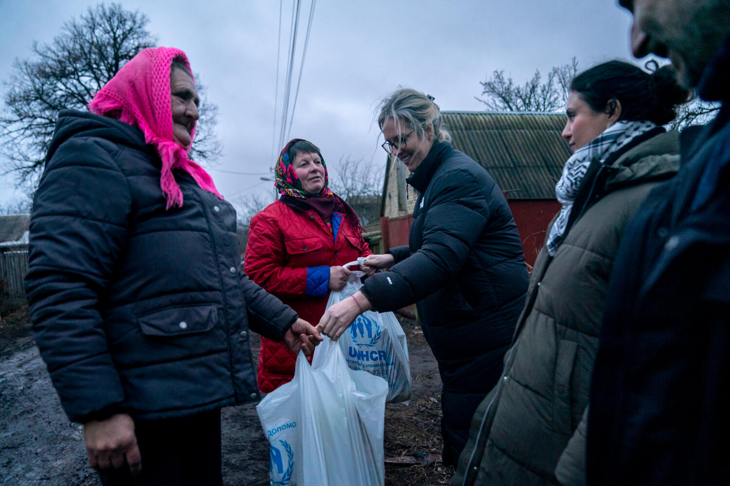 Dos mujeres ucranianas reciben bolsas de alimentos y otros artículos de ayuda de miembros del personal de ACNUR.