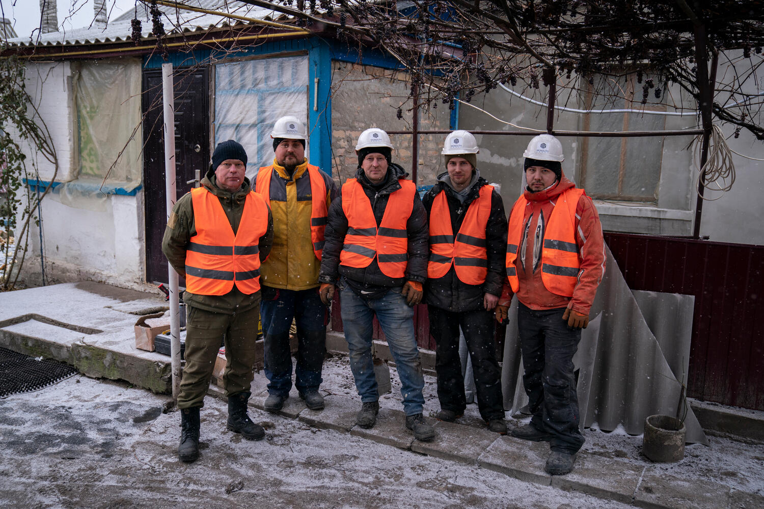 Un grupo de trabajadores de construcción con chalecos reflectantes frente a una casa parcialmente dañada en Ucrania.