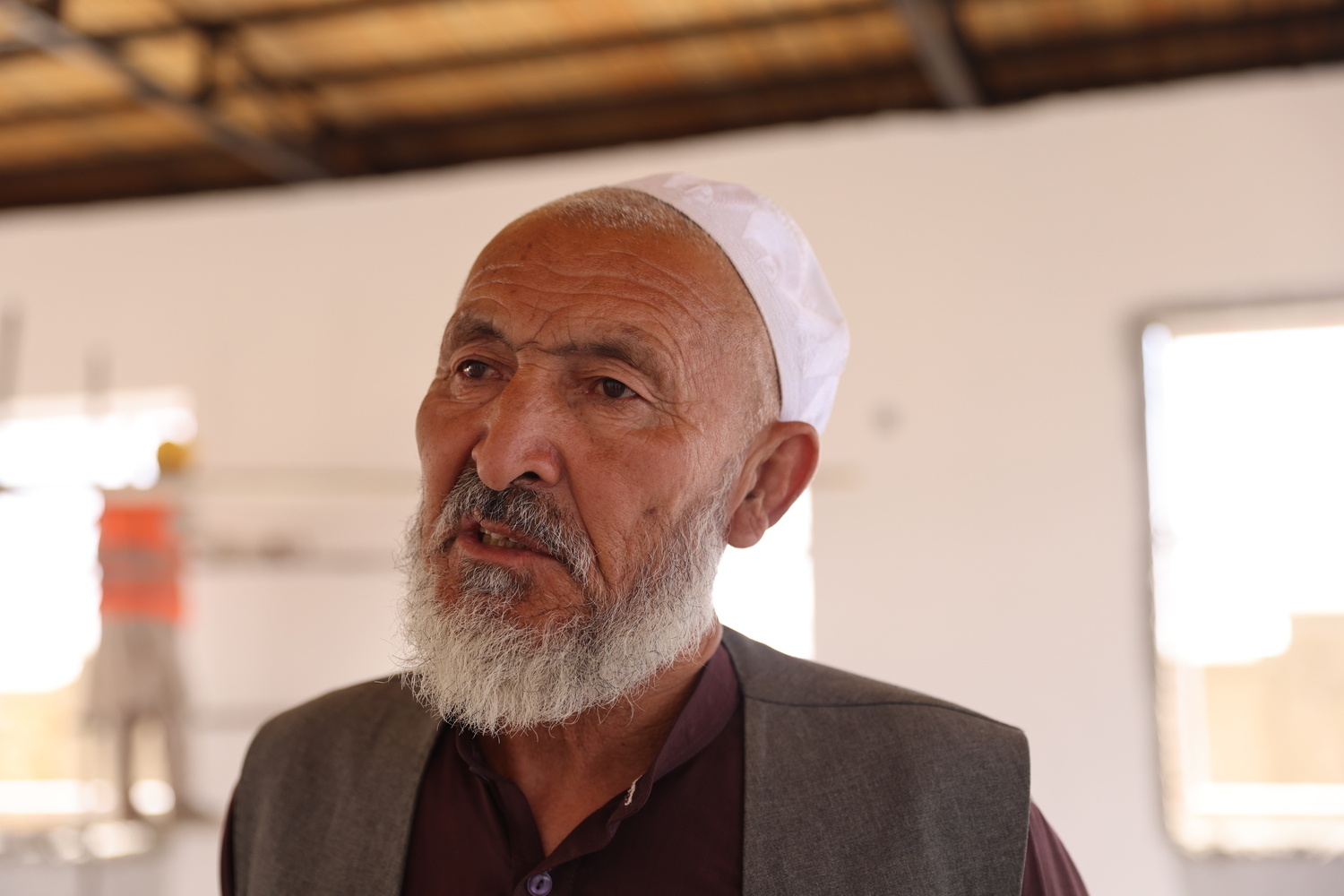 Un hombre mayor con barba y fez blanco habla con alguien fuera de cámara.
