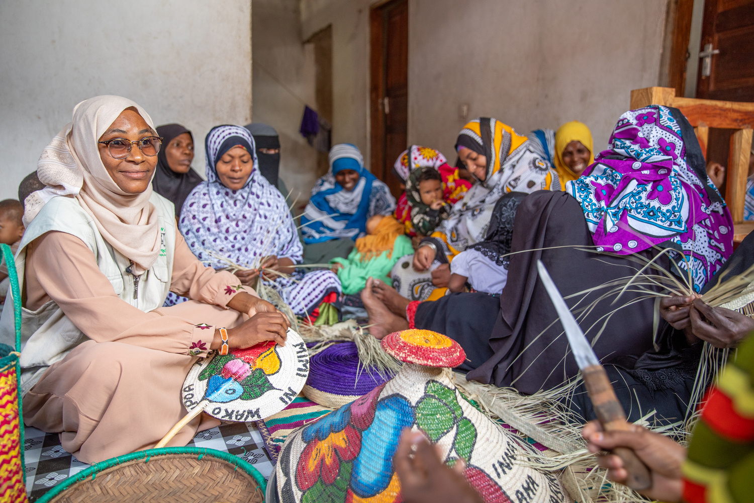 Un grupo de mujeres sentadas en el suelo tejen cestas de colores.