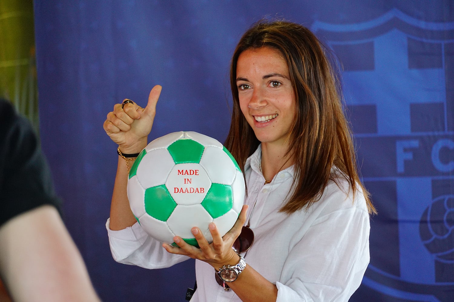 Aitana Bonmatí muestra un balón de fútbol sonriendo y con su pulgar arriba.