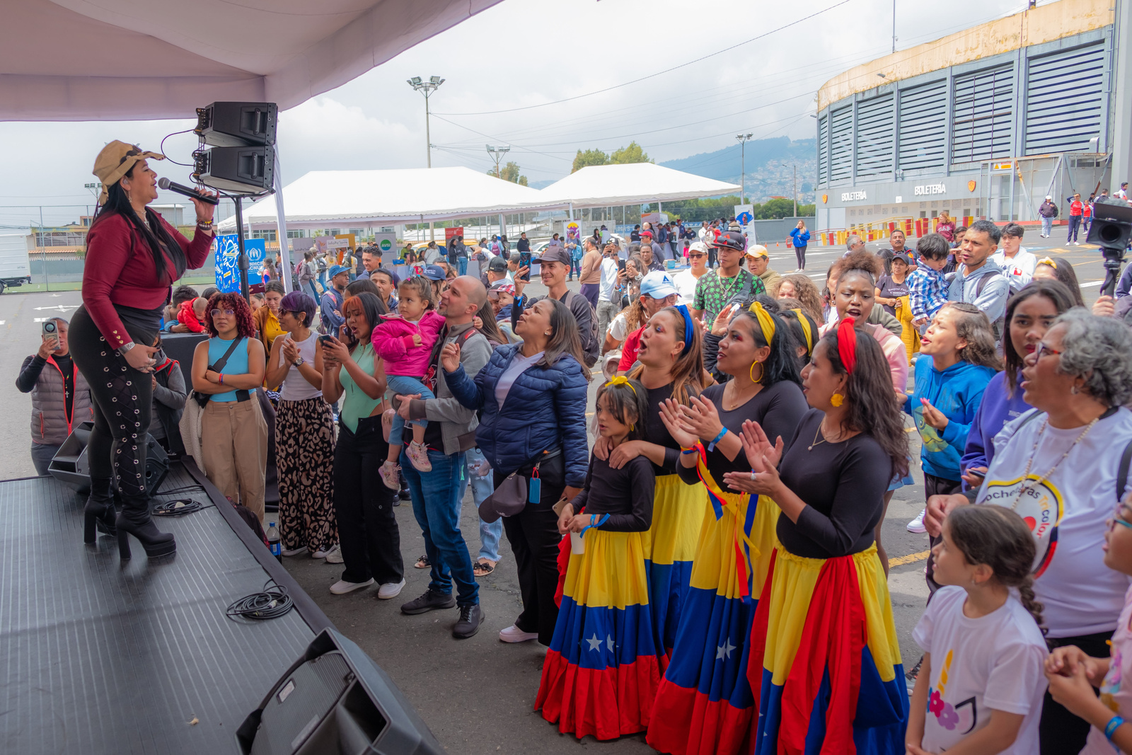 Una mujer vestida de rojo y negro, que porta sombrero, canta frente a un público