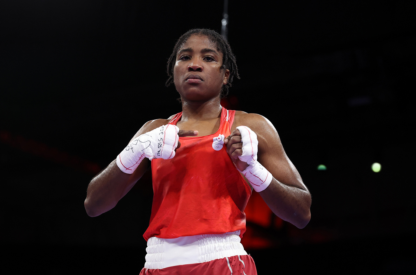 Una mujer posa para una foto con ropa de boxeo color rojo, señalando el logotipo del Equipo Olímpico de Atletas efugiados en su ropa.
