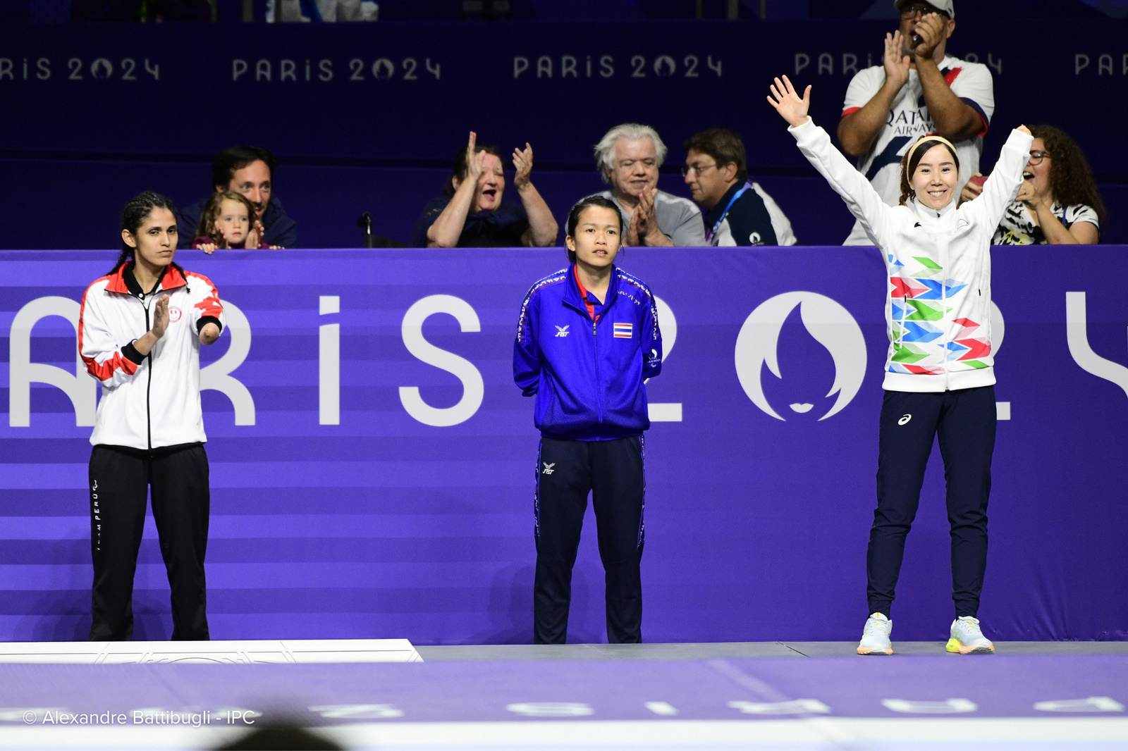 Una atleta levanta los brazos en señal de celebración mientras otras dos celebran con la mirada