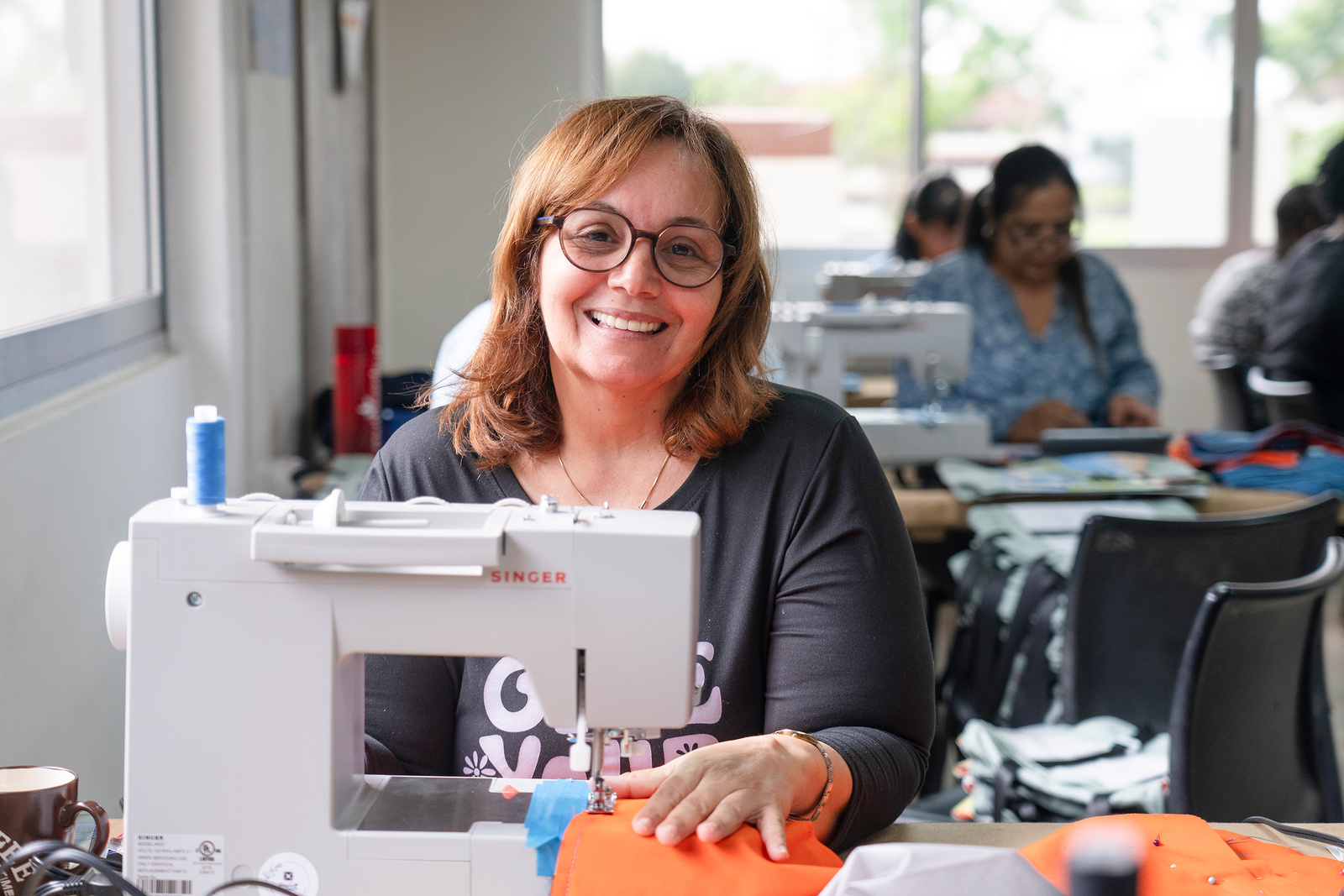 Una mujer de cabello rubio posa frente a una máquina de coser
