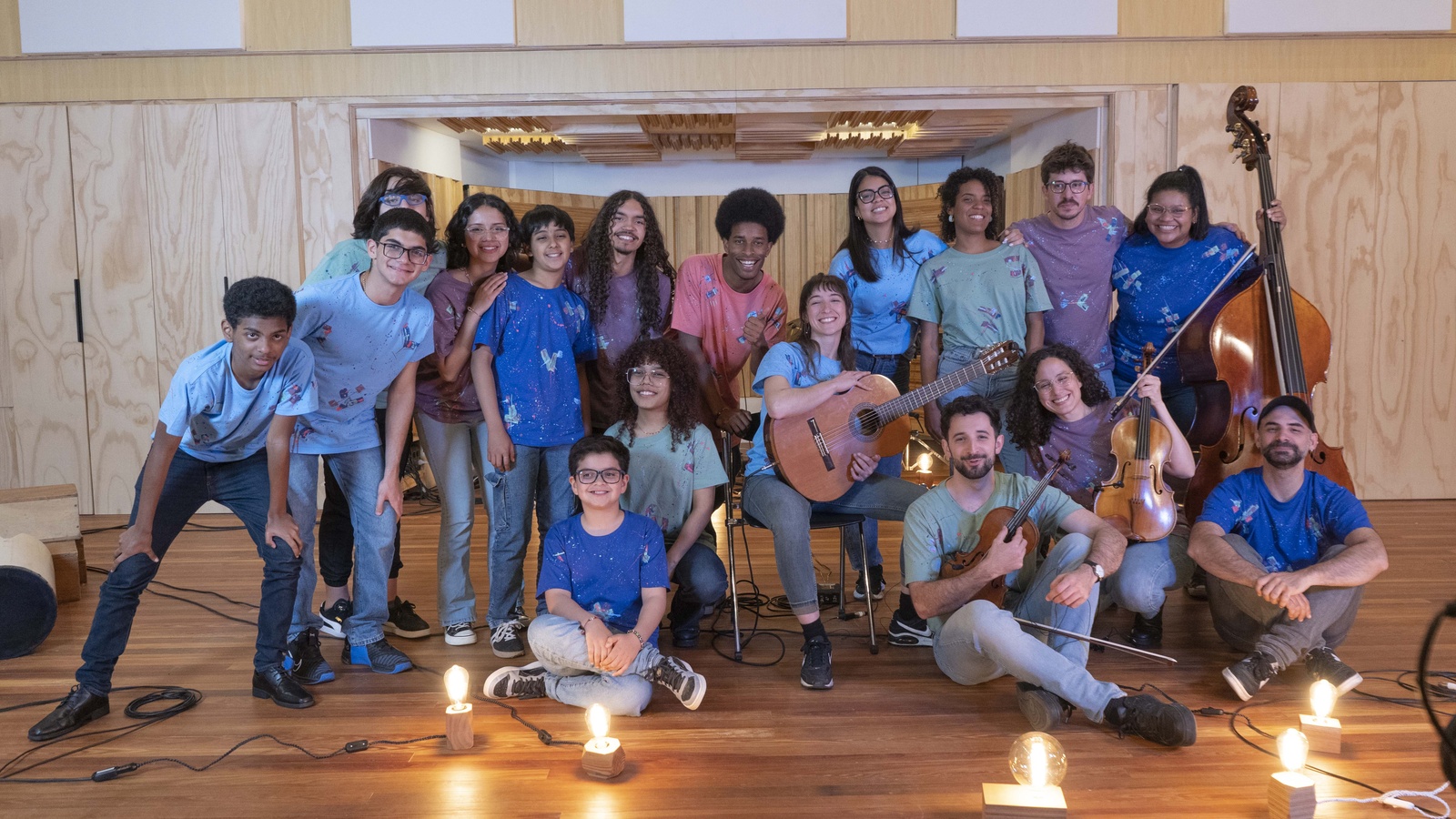 Un grupo de 17 personas, en su mayoría adolescentes y jóvenes, posan con instrumentos musicales en un estudio de grabación